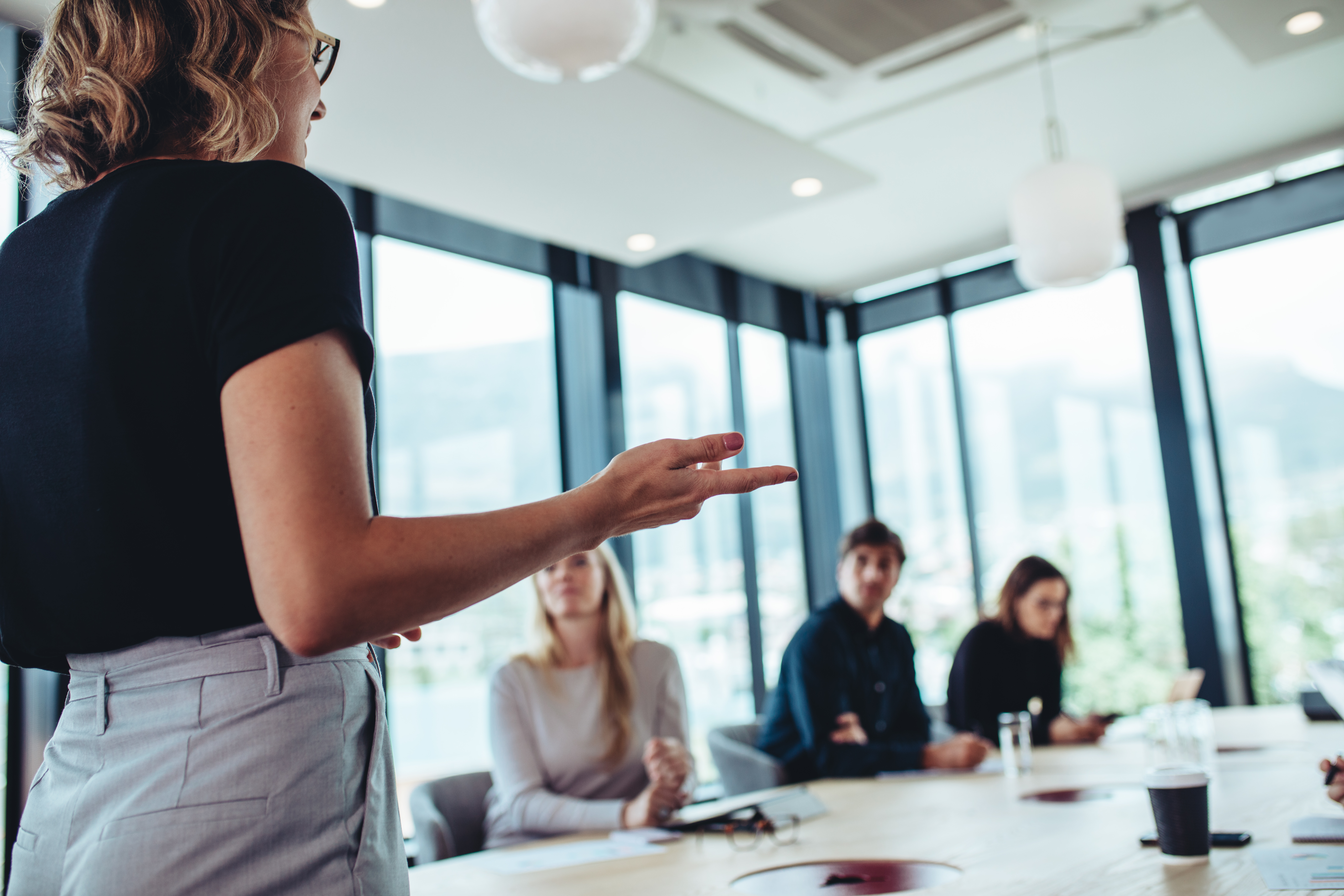Depth of field image of a blond woman presenting to a conference room of people